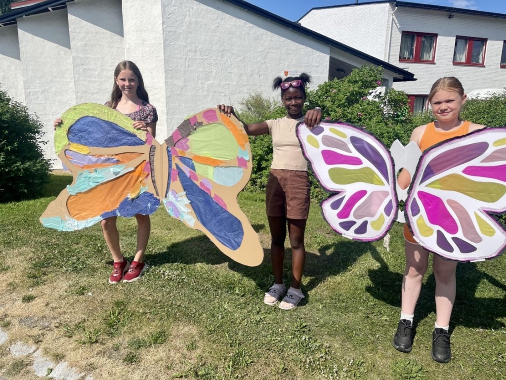 Fra venstre Isabell, Phiona og Frida, med noen av de store sommerfuglene som skal ønske Little Amal velkommen.